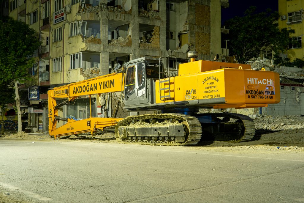 pexels photo 17171336 17171336 Large excavator at a city demolition site during nighttime, illuminated by streetlights.