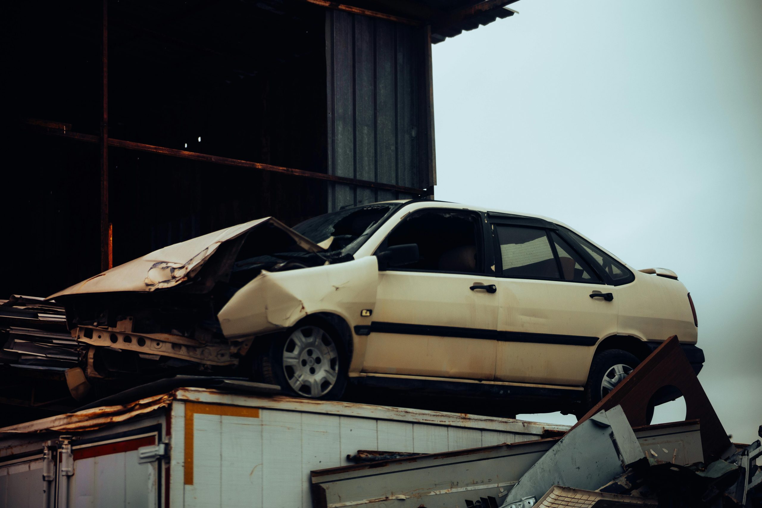 A damaged car sits atop a metal scrap heap, showing a scene of automotive decay.