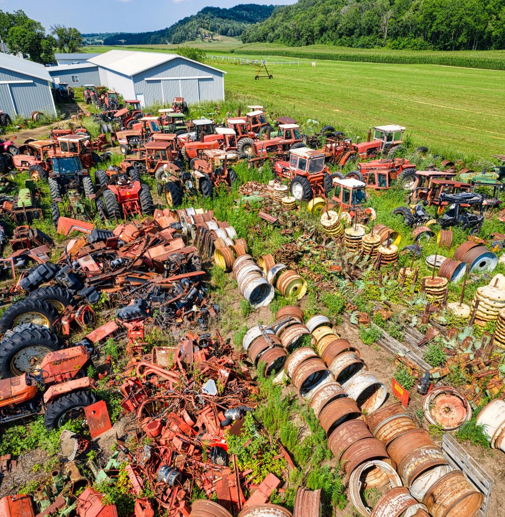 pexels photo 9642551 9642551 Aerial shot of abandoned tractors and machinery in a rustic junkyard amidst green fields.